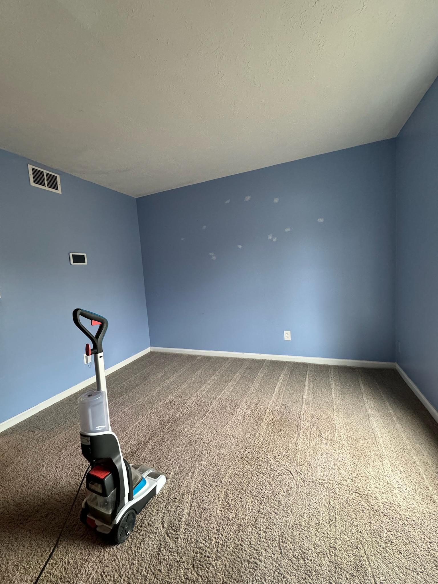 A carpet shampooer part-way through a room, cleaned carpet behind it