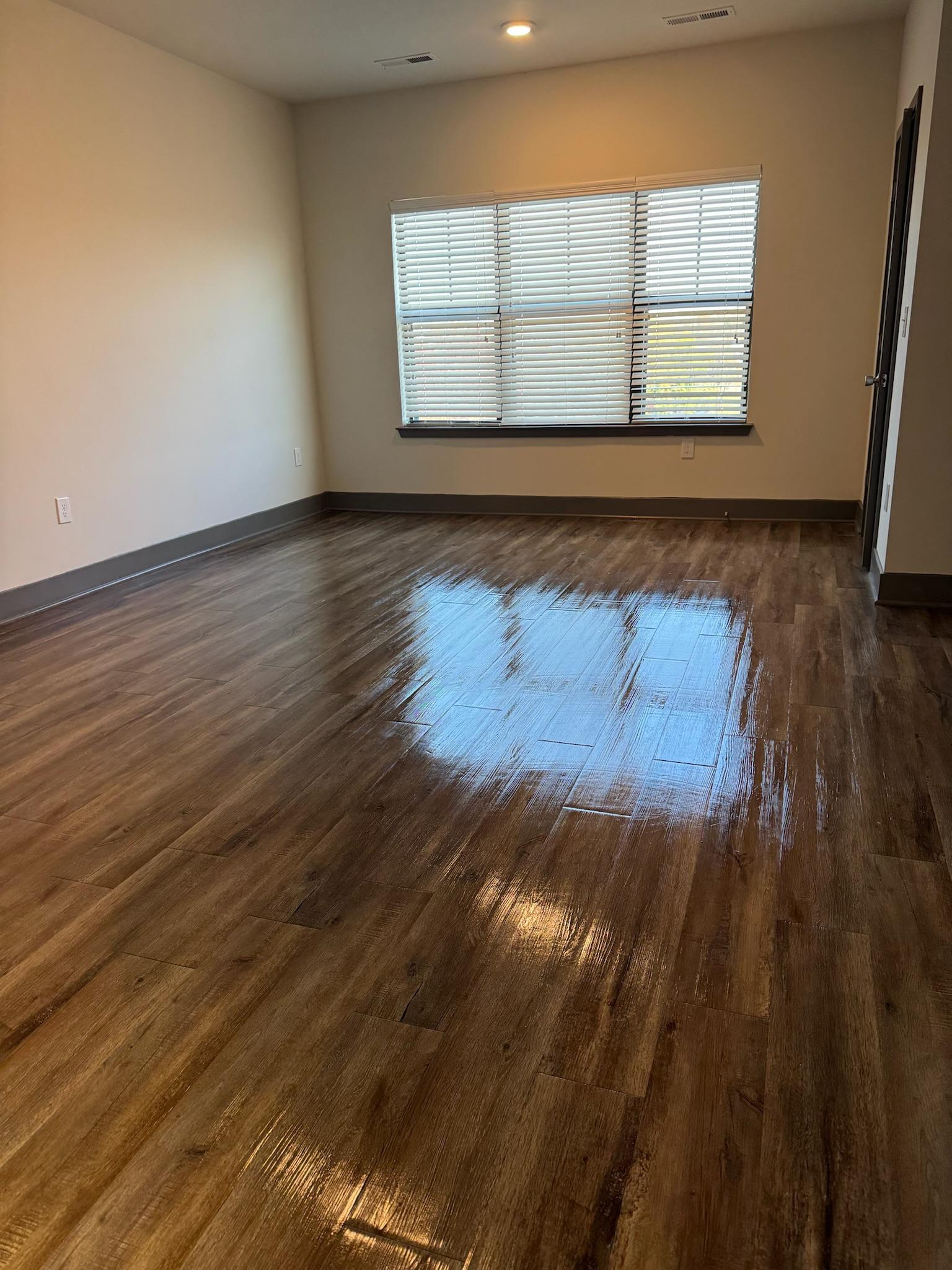 A freshly mopped hardwood floor in an empty room, catching the light from the window